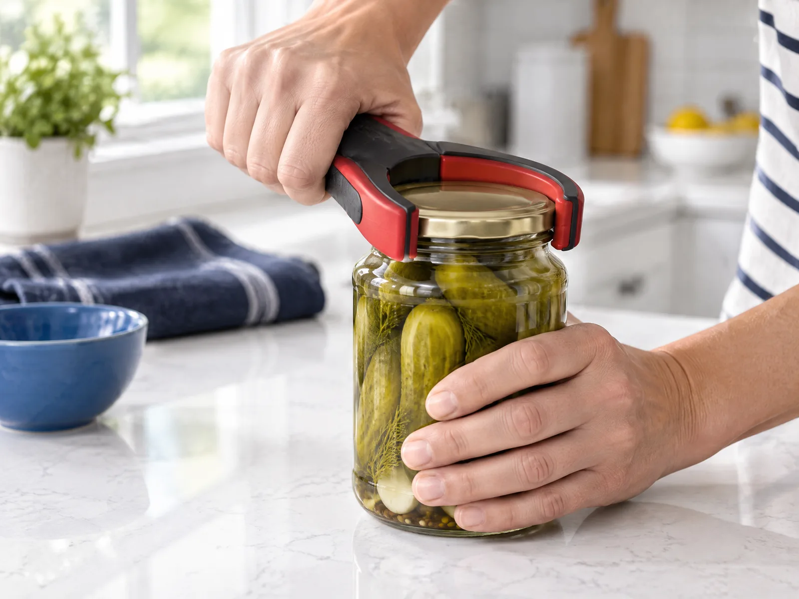 Hands twisting open a jar of pickles with a red and black jar-opening tool on a kitchen counter